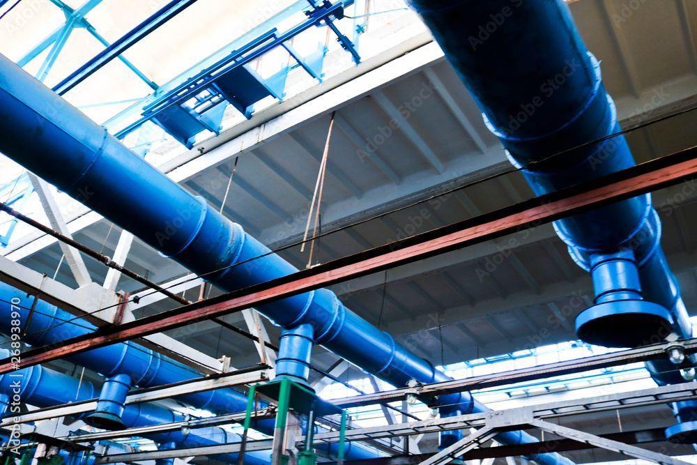 The ceiling in the workshop at the industrial chemical petrochemical machine-building refinery with blue metal iron large pipes of inlet and exhaust ventilation