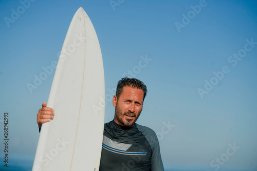 handsome and attractive surfer man in neoprene swimsuit holding surf board posing cool after surfing enjoying Summer water sport and holidays
