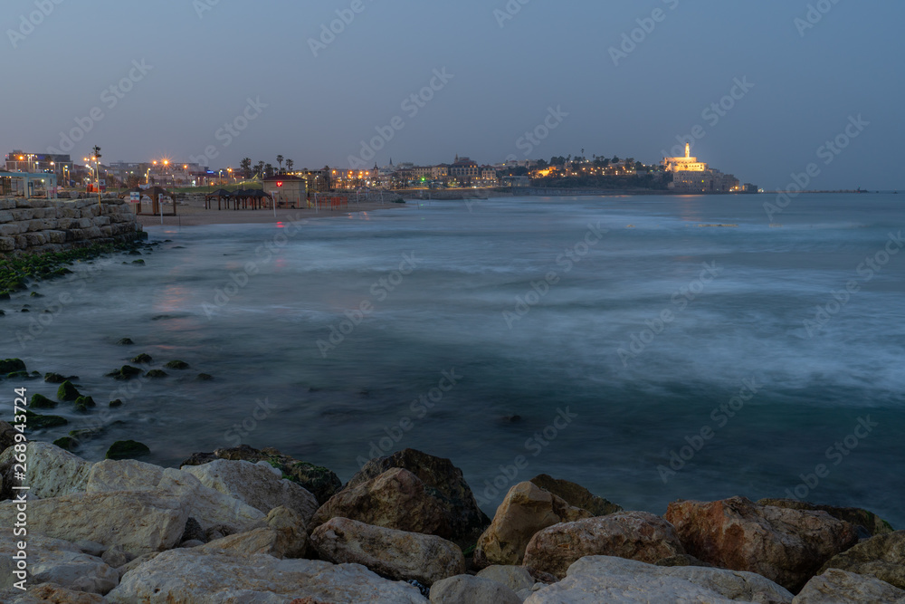 A pre dawn image of a church on a hill of an old city across the sea.