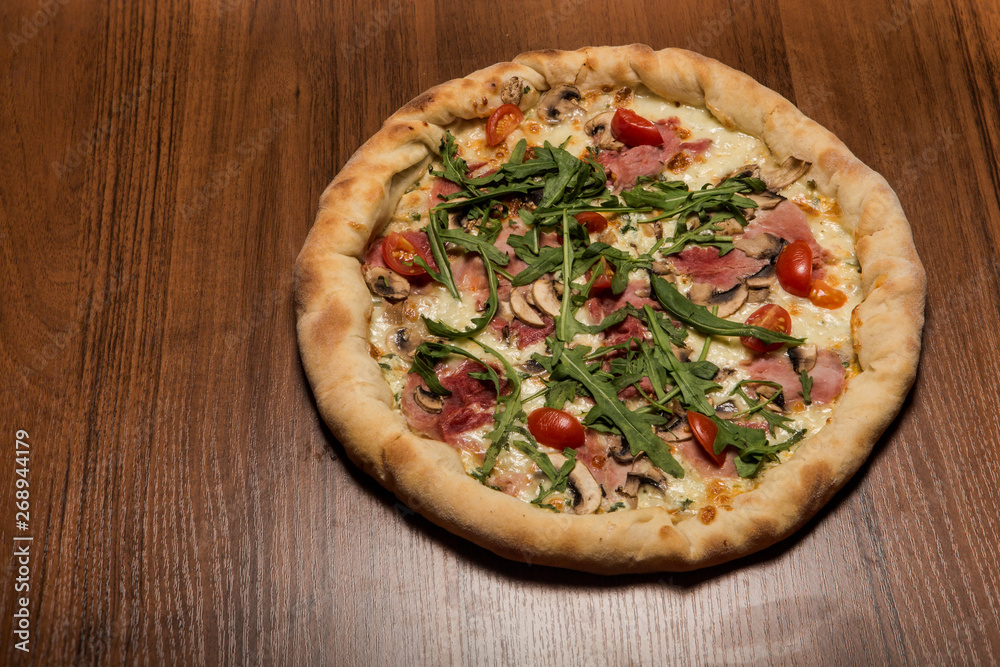 delicious whole pizza with arugula, ham, mushrooms and tomatoes