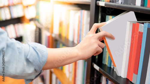 Bestseller publishing concept. Male hand choosing and picking white book from wooden bookshelf in bookstore. Education research in university public library. photo