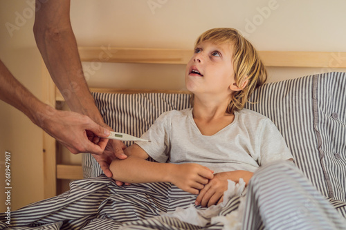 Sick boy with thermometer laying in bed and father hand taking temperature. father checking temperature of her sick son who has thermometer. Sick child with fever and illness in bed