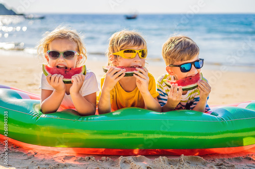 Children eat watermelon on the beach in sunglasses