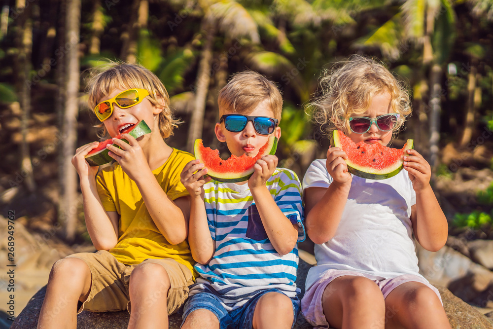 Children eat watermelon on the beach in sunglasses Children eat watermelon on the beach in sunglasses