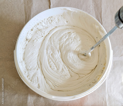 White acrylic glazing putty stirred in a bucket. Thick texture.