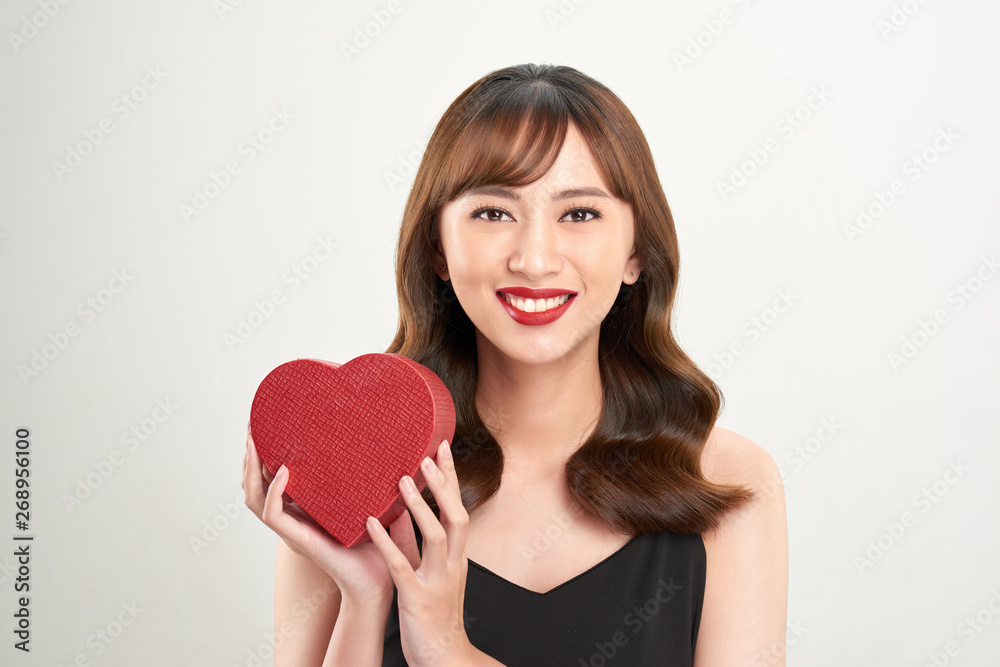 Cute young woman holding pink heart symbol against pale white background Cute young woman holding pink heart symbol against pale white background