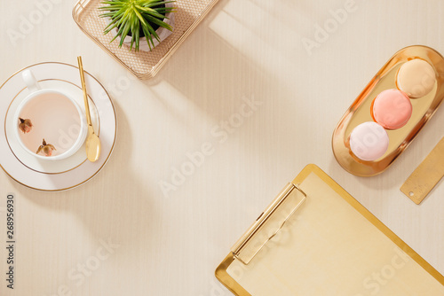 Modern gold stylized home office desk with folder, macaroons, coffee mug on beige background. Flat lay, top view lifestyle concept. photo