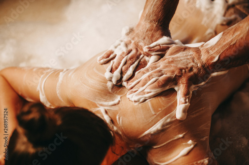 Upper view hands of a male masseur doing a foam massage for skin cleaning to a dark haired woman in a spa center. photo