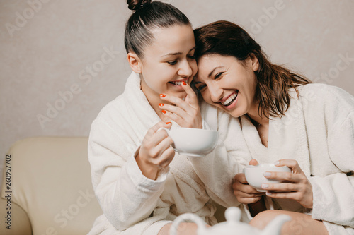 Tableau sur toile Two beautiful girlfriends having fun dressed in bathrobes after spa procedures laughing while one is leaning her head her girlfriend