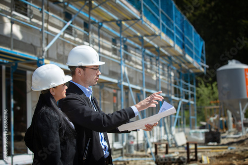 Two architects a man and a woman in construction in white helmets.