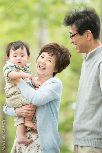 新緑の中で孫を抱き微笑む祖父母
