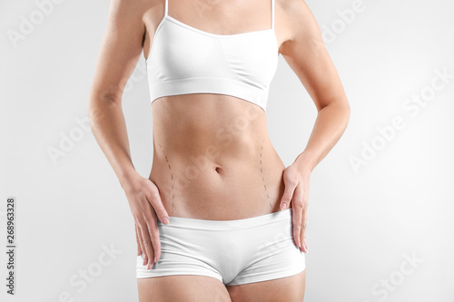 Young woman with marks on her belly against light background. Concept of plastic surgery © Pixel-Shot