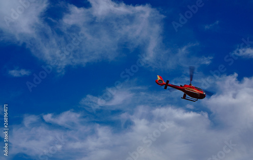 Fototapeta Naklejka Na Ścianę i Meble -  Red helicopter flying with blue sky and white clouds in background