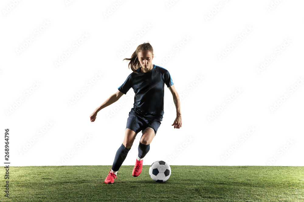 Young female football or soccer player with long hair in sportwear and boots kicking ball for the goal in jump isolated on white background. Concept of healthy lifestyle, professional sport, hobby.