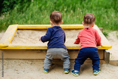 The two-year-old twin brothers play together on the playground. They are dressed in bright colors.