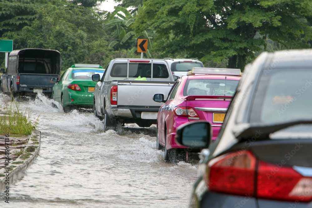 The line of cars ride on a road under water. Flood on the street. The line of cars ride on a road under water. Flood on the street.
