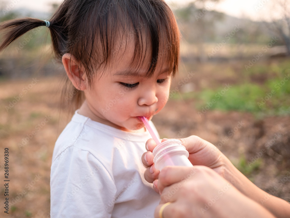 Asian little child girl drink water from tube after tired of playing in the garden with mother. Asian little child girl drink water from tube after tired of playing in the garden with mother.