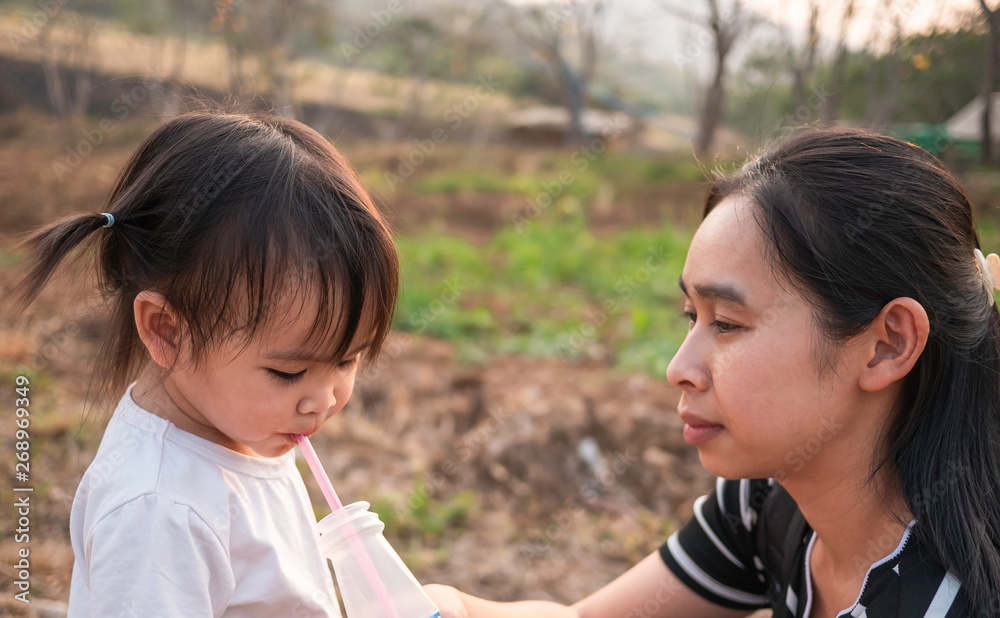 Asian little child girl drink water from tube after tired of playing in the garden with mother. Asian little child girl drink water from tube after tired of playing in the garden with mother.
