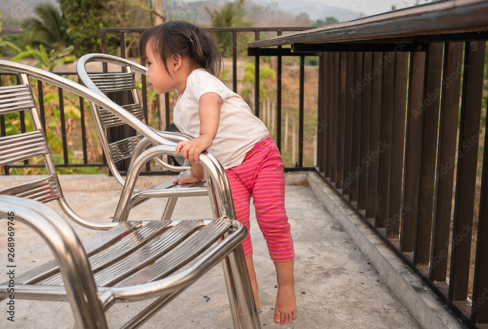 Asian little child try to climb down the chair by herself, Dangerous in children. Education and self-development concept.