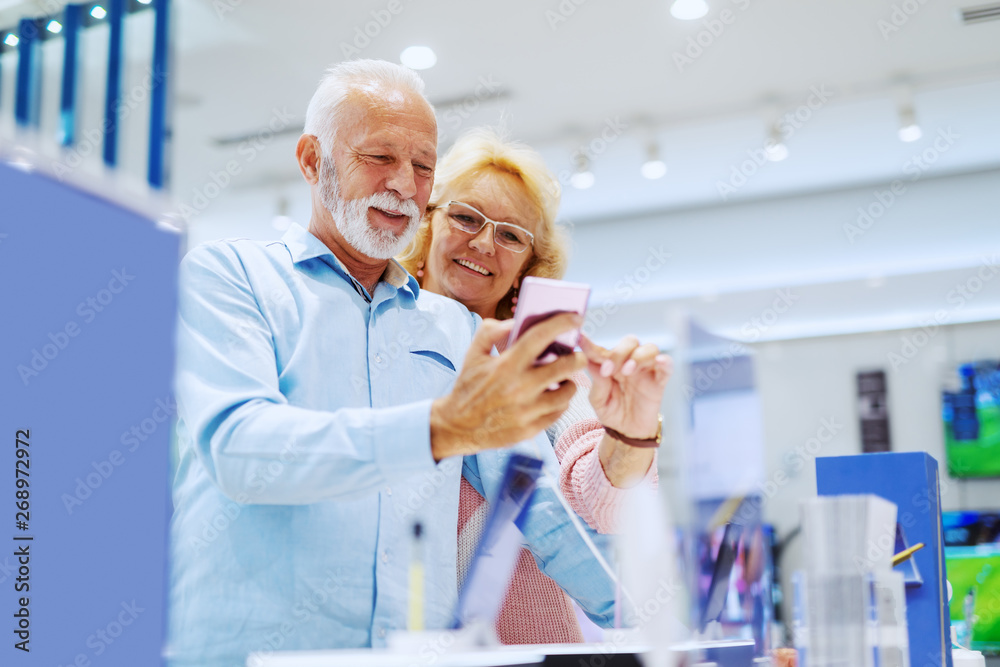 Cute smiling senior couple standing in tech store and choosing new smart phone. Cute smiling senior couple standing in tech store and choosing new smart phone.