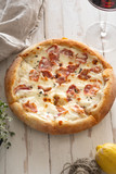 Top view image of cooked pizza with bacon, cheese and thyme served with a glass of wine on white wooden distressed table