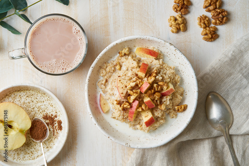 Oatmeal with apple, nuts, honey and cup of chocolate on white wooden light background. Top view. Healthy diet breakfast