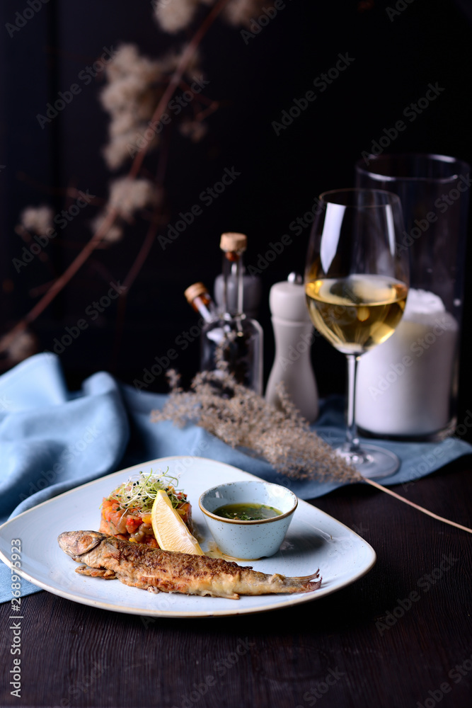 grilled fish with vegetables and lemon on the background of a glass of white wine