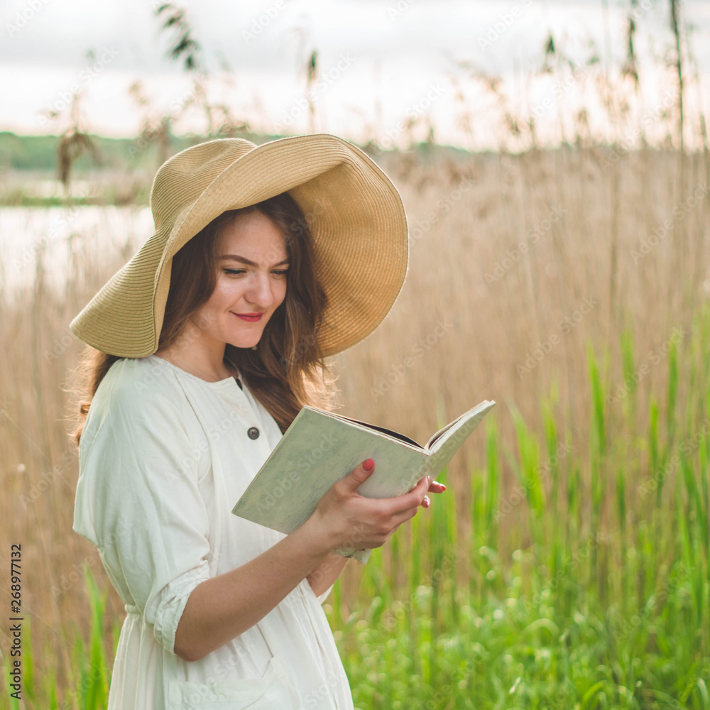 Beautiful girl in field reading a book. The girl sitting on a grass, reading a book. Rest and reading. Outdoor reading.