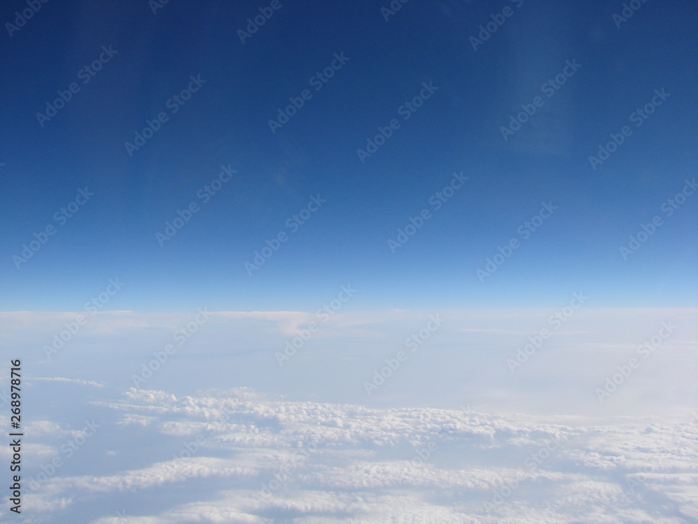 Panorama of an infinite snow-white cloudy field on the background of sky blue on the horizon, opens from the window of the plane.