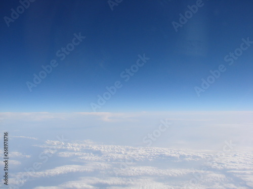 Panorama of an infinite snow-white cloudy field on the background of sky blue on the horizon, opens from the window of the plane. © Hennadii