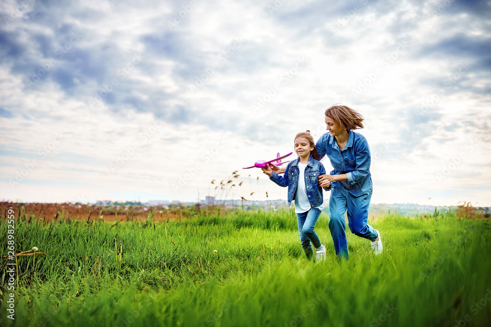 Young woman and girl in denim clothes having fun with small plane on green lawn in summer day Young woman and girl in denim clothes having fun with small plane on green lawn in summer day