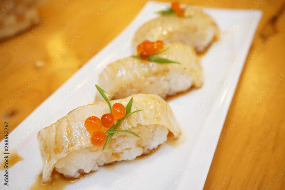 Aburi engawa sushi - Grilled flatfish (Fluke fin) on rice topping with salmon roe (Ikura) served with wasabi and pickled ginger, Japanese traditional food. Aburi engawa sushi - Grilled flatfish (Fluke fin) on rice topping with salmon roe (Ikura) served with wasabi and pickled ginger, Japanese traditional food.