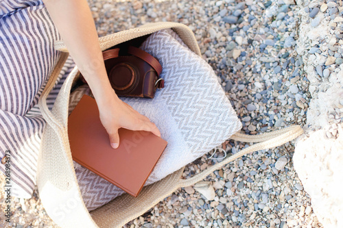 Woman takes paper book from straw bag at sea beach. Girl is enjoying summer vacation, reading and traveling. Tourist is relaxing in holidays.