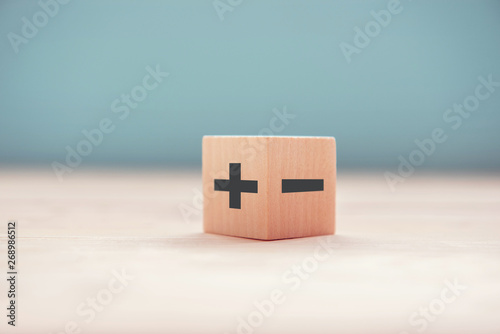 The concept of opposites, wood blog with plus and minus on blue background, flat lay, copy space.