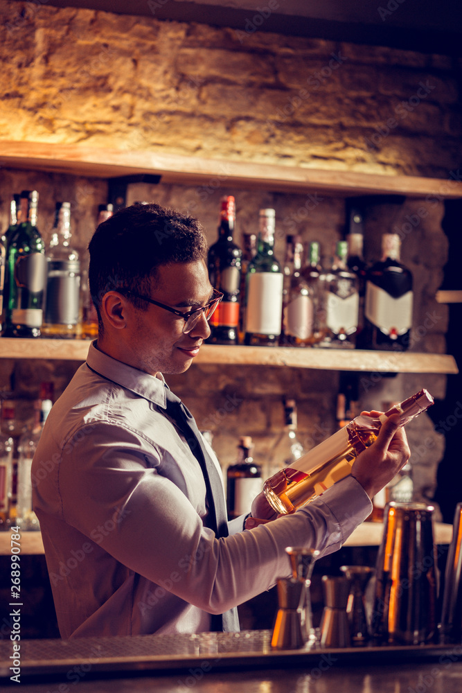 Dark-haired owner of bar holding bottle of whisky