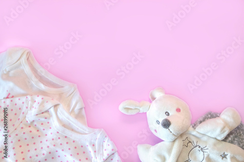 Beautiful set baby accessories - newborn baby clothes and funny toys on pink background. Copy space, flat lay, top view.