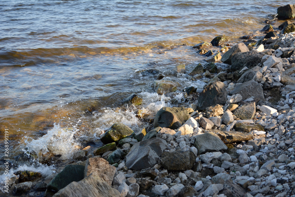 Beautiful view of sea waves hitting stones and pebbles on the beach on the sunset.