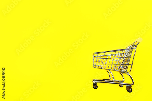 Toy cart for products on a yellow background. Place for text. View from above. The concept of shopping and consumption