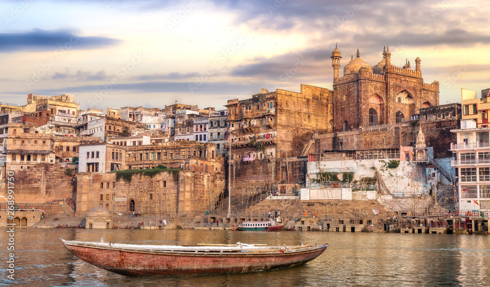 Ancient Varanasi city architecture at sunset with view of Ganges river ghat and wooden boat on river Ganga