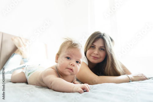 Mother with her newborn son lay on the bed in the rays of sunlight coming out of the window .