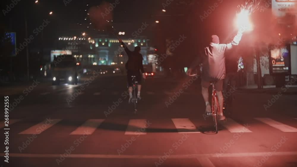 Group of male people cyclists with burning red signal flare at night city street. Protest and creative democracy. Active lifestyle. Ecological urban transport. Freedom concept