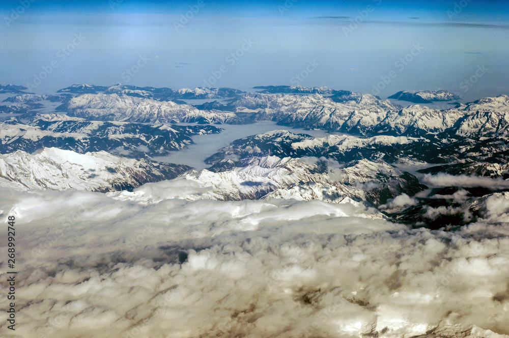 Aerial view of snowy mountains in winter. Flying above the clouds.