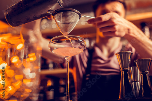 Barman pouring juice into glass while using sieve