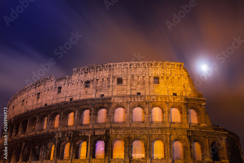 Dettaglio del Colosseo di notte con la luna piena in lunga esposizione  e finestre infuocate