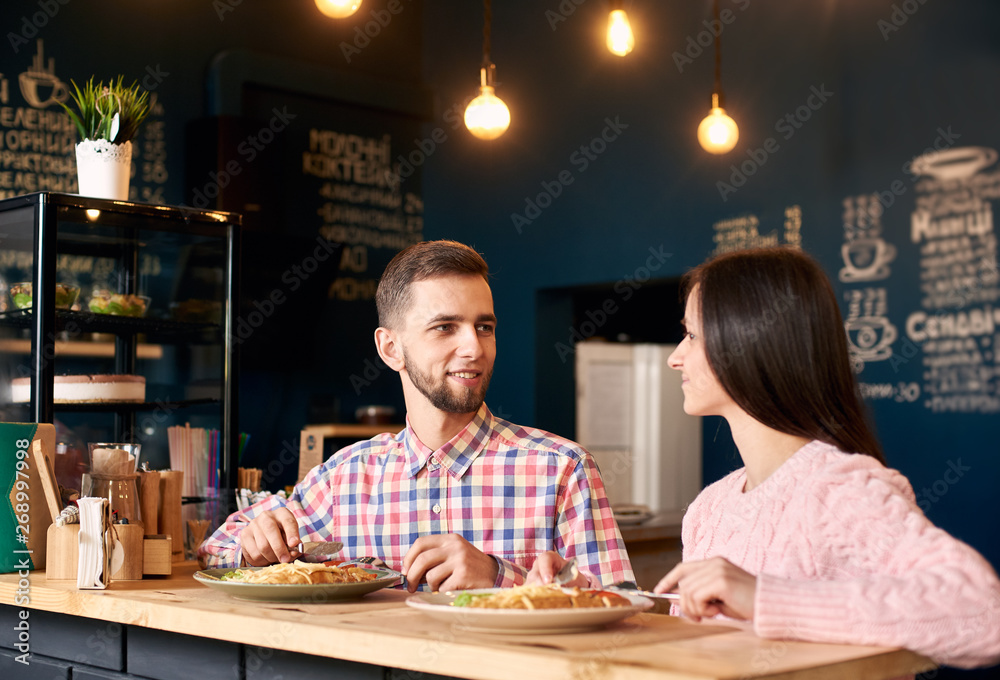 Two people in cafe enjoying time spending with each other, nice moment during breakfast. Woman in pink sweater and man in chequered shirt having fun talking and having lunch of delicious food in cafe. Two people in cafe enjoying time spending with each other, nice moment during breakfast. Woman in pink sweater and man in chequered shirt having fun talking and having lunch of delicious food in cafe.