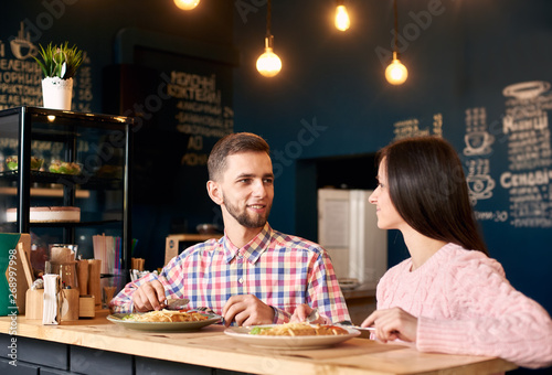 Two people in cafe enjoying time spending with each other  nice moment during breakfast. Woman in pink sweater and man in chequered shirt having fun talking and having lunch of delicious food in cafe.