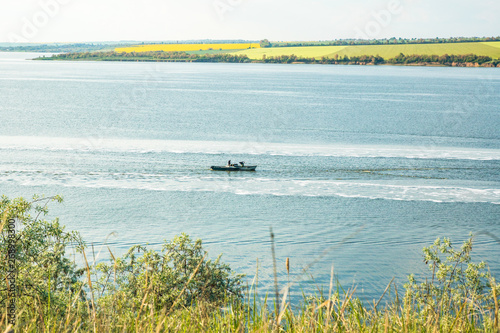 Fotografija fishing motor boat is trawl in the lake, green fields on the background