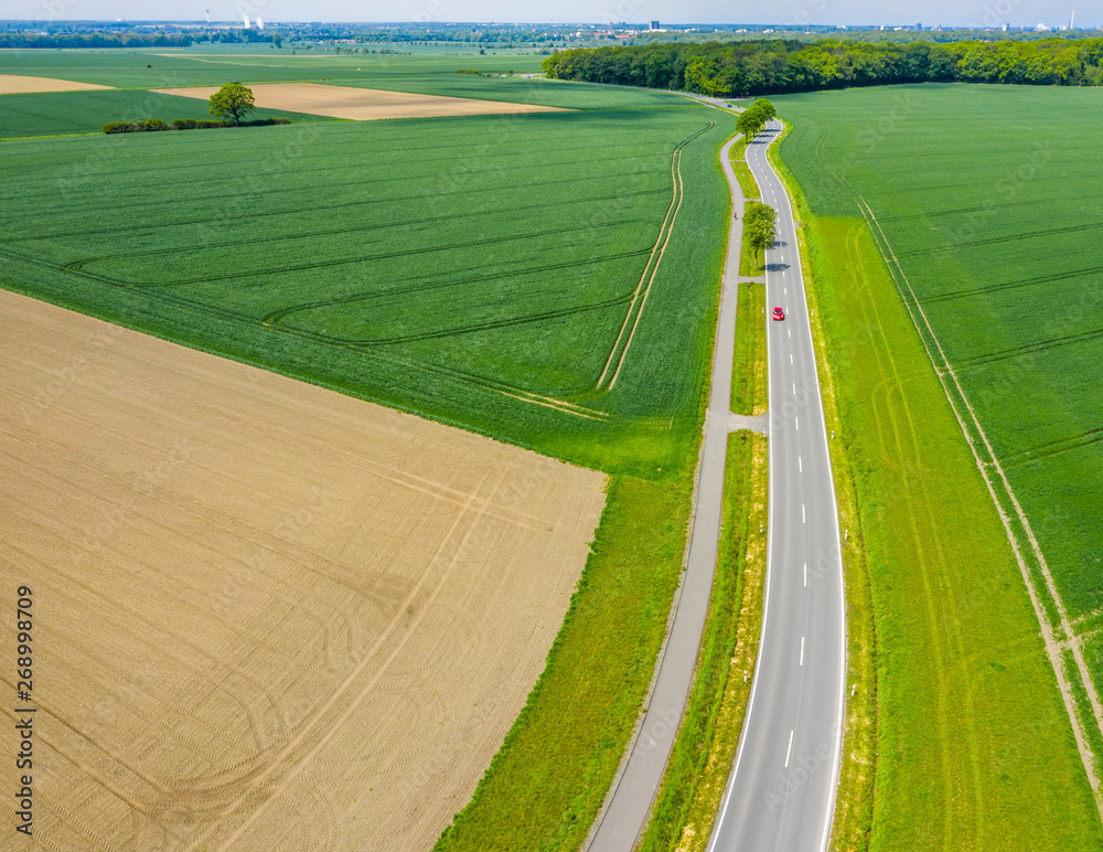 Aerial photograph with the drone camera of a small asphalted country road leading through fields and meadows, drone shot