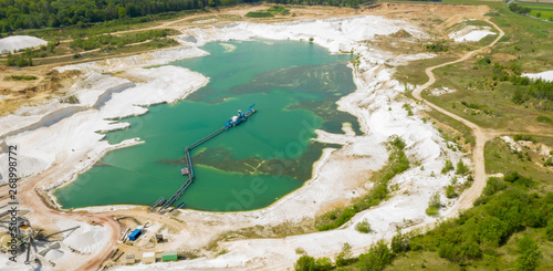 Aerial view of a blue-green quarry pond for quartz sand in Germany with the suction dredger and the conveyor belt for the sand, minng