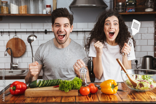 Excited cheerful young couple cooking healthy salad photo